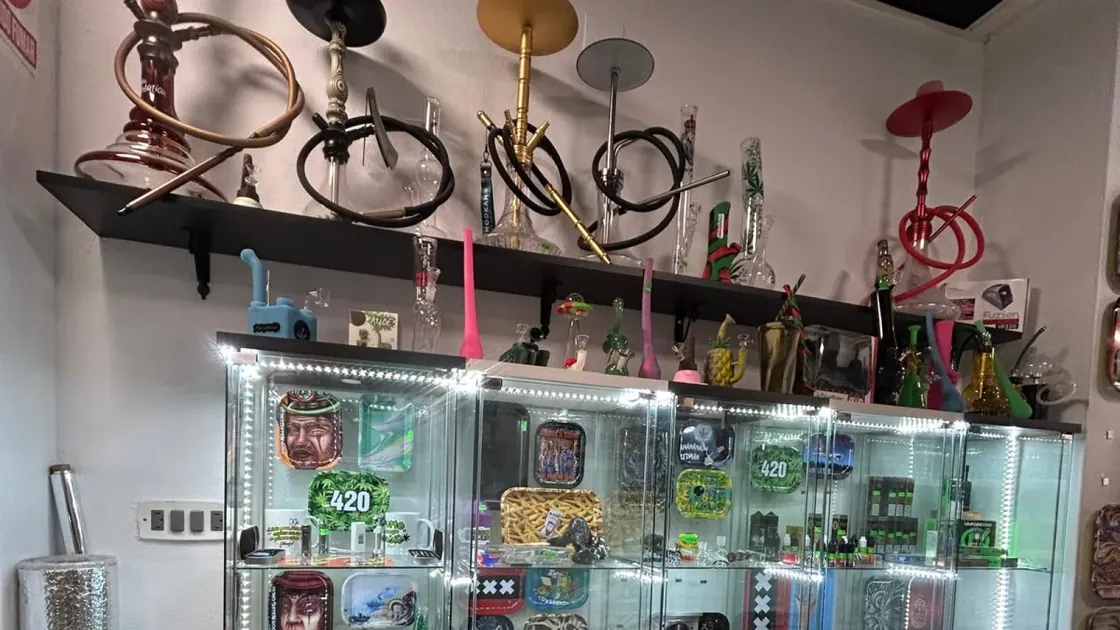 Vitrina iluminada con parafernalia: cachimbas y pipas de cristal en el estante superior, cajas y accesorios dentro